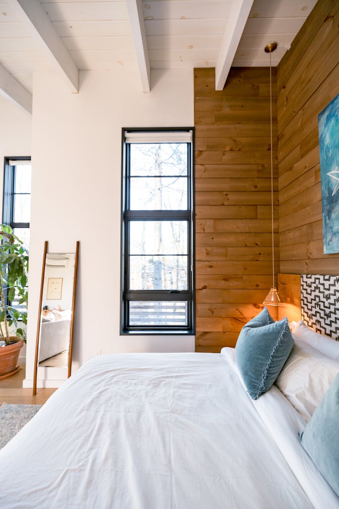 A stylish bedroom featuring a wood accent wall, minimalist decor, and ample natural light.